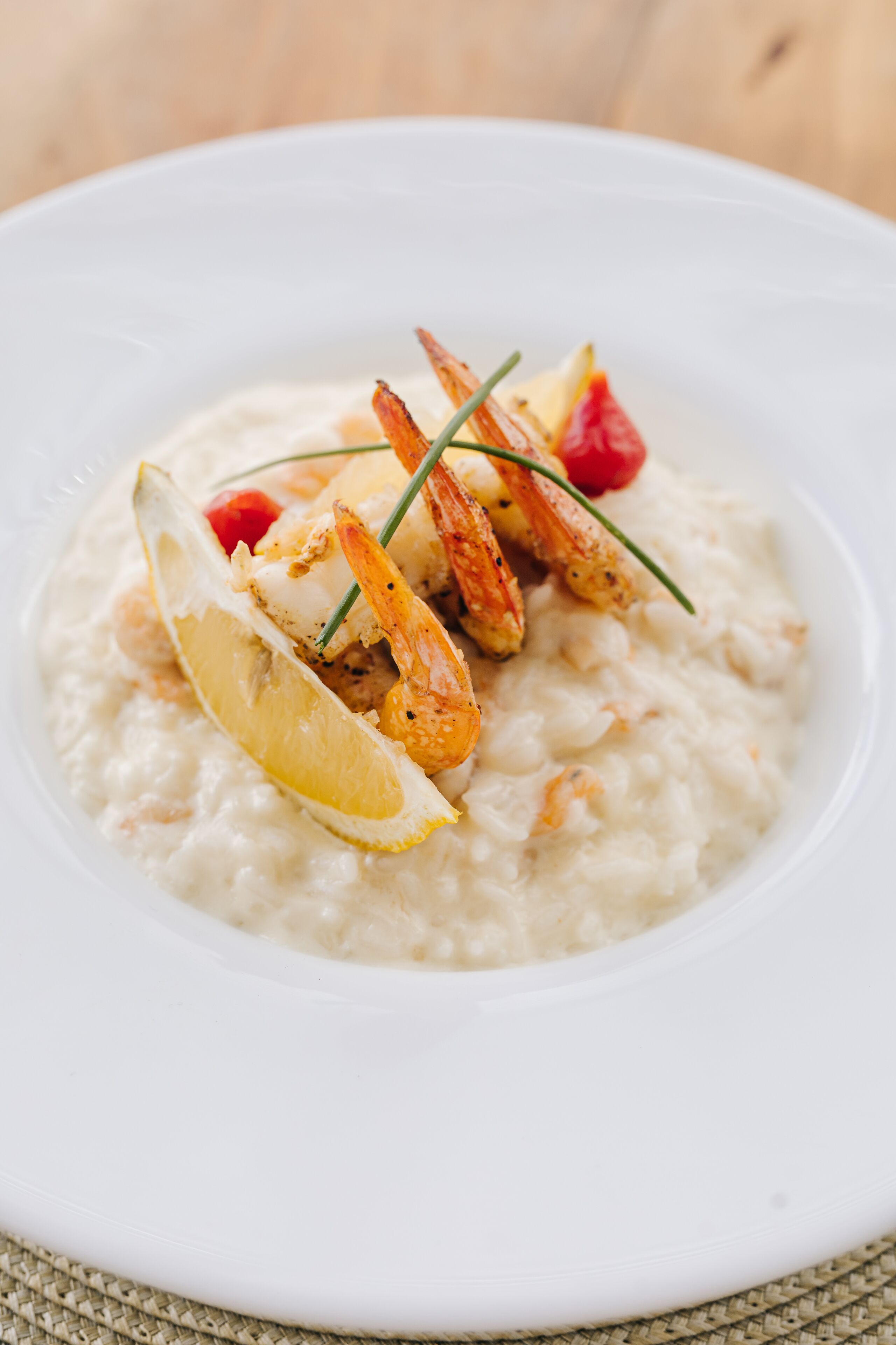 Un plato blanco con un guiso de mariscos, posiblemente risotto, adornado con limón y hierbas.