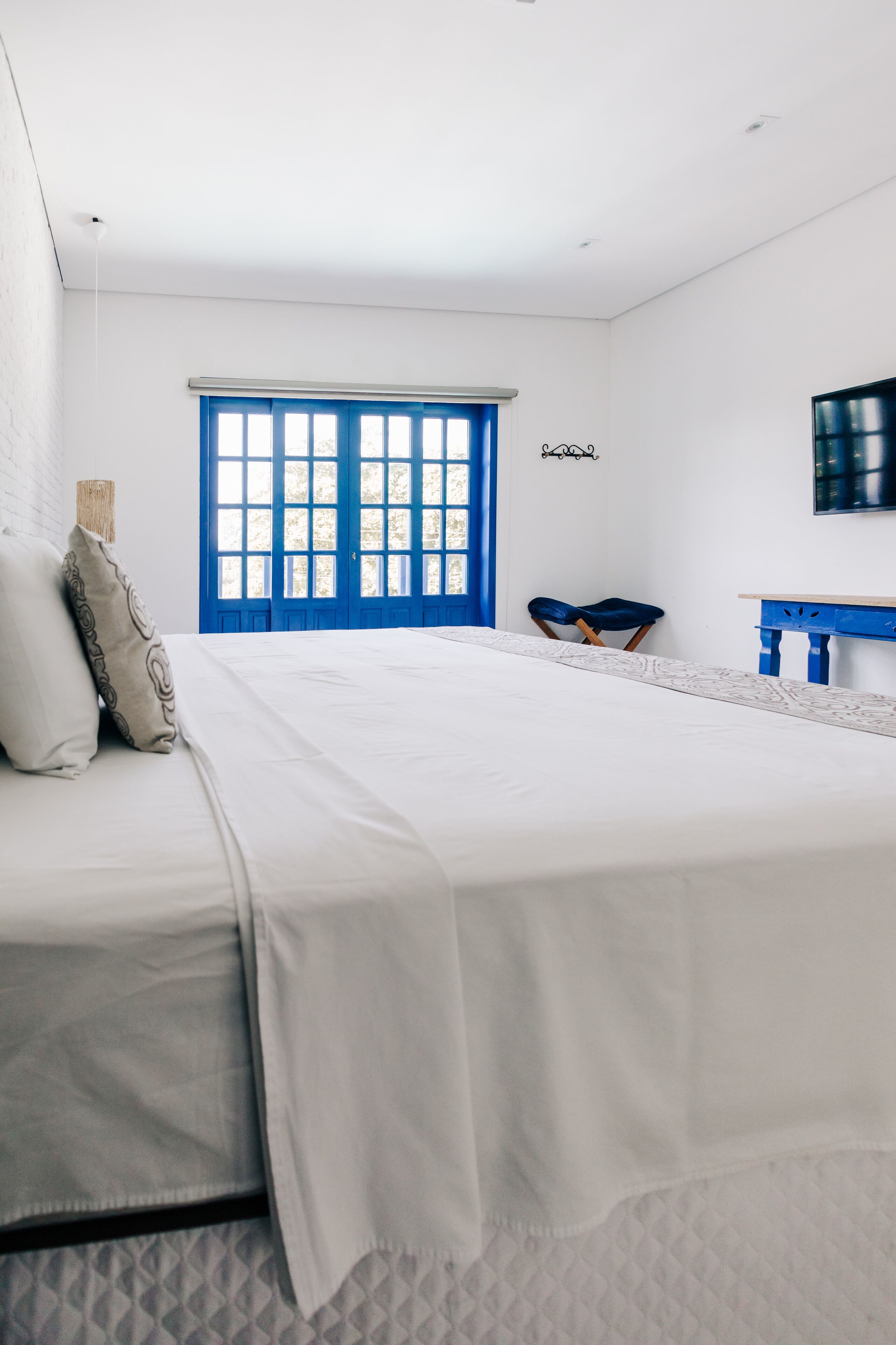 A bedroom with a large bed, a blue door, a small table, and a TV on the wall.