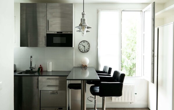 Una cocina moderna con electrodomésticos de acero inoxidable, un comedor con mesa negra y una ventana con vistas a zonas verdes.