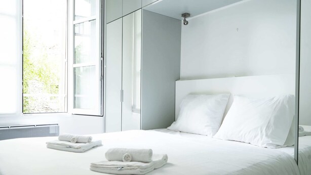 Een moderne slaapkamer met een groot bed, witte lakens en een raam met uitzicht op groen.