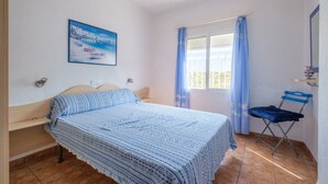 Une chambre à coucher avec un lit, une fenêtre avec des rideaux, une chaise et un tableau accroché au mur.