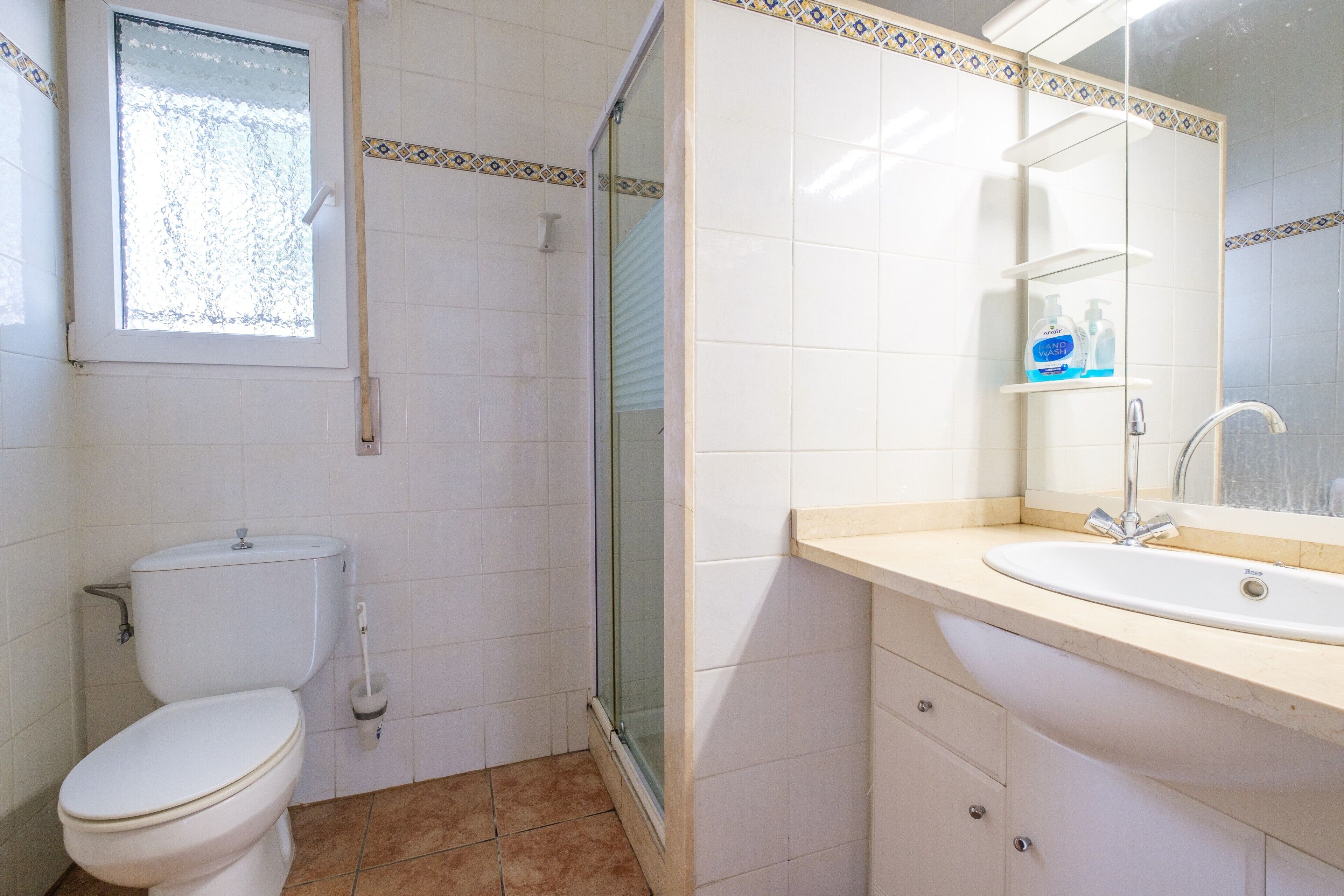 Een badkamer met een toilet, een douchecabine van glas, een wastafel met spiegel en een raam.
