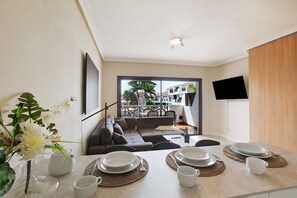 Un espace repas moderne avec une table dressée pour quatre personnes, un canapé et une vue sur l’extérieur.