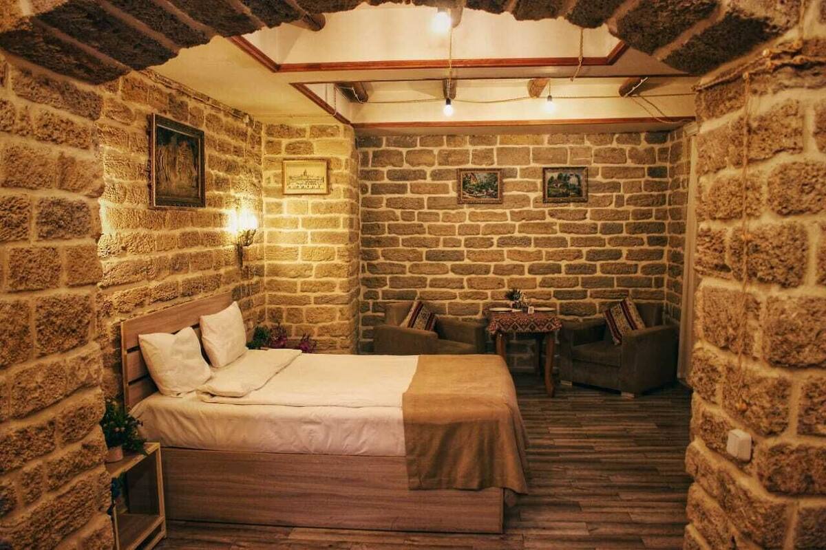 Een kamer met een bed, twee stoelen, een kleine tafel en stenen muren.