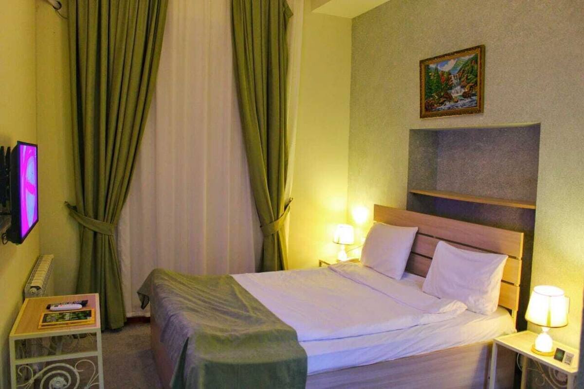Hotelkamer met een bed, twee bedlampen, een televisie, een klein tafeltje met een afstandsbediening, en een schilderij aan de muur.