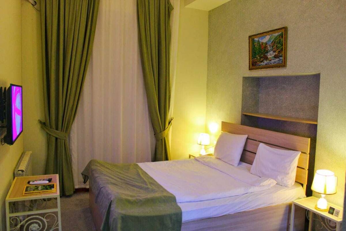 Een hotelkamer met een bed, twee bedlampjes, een televisie en een schilderij aan de muur.