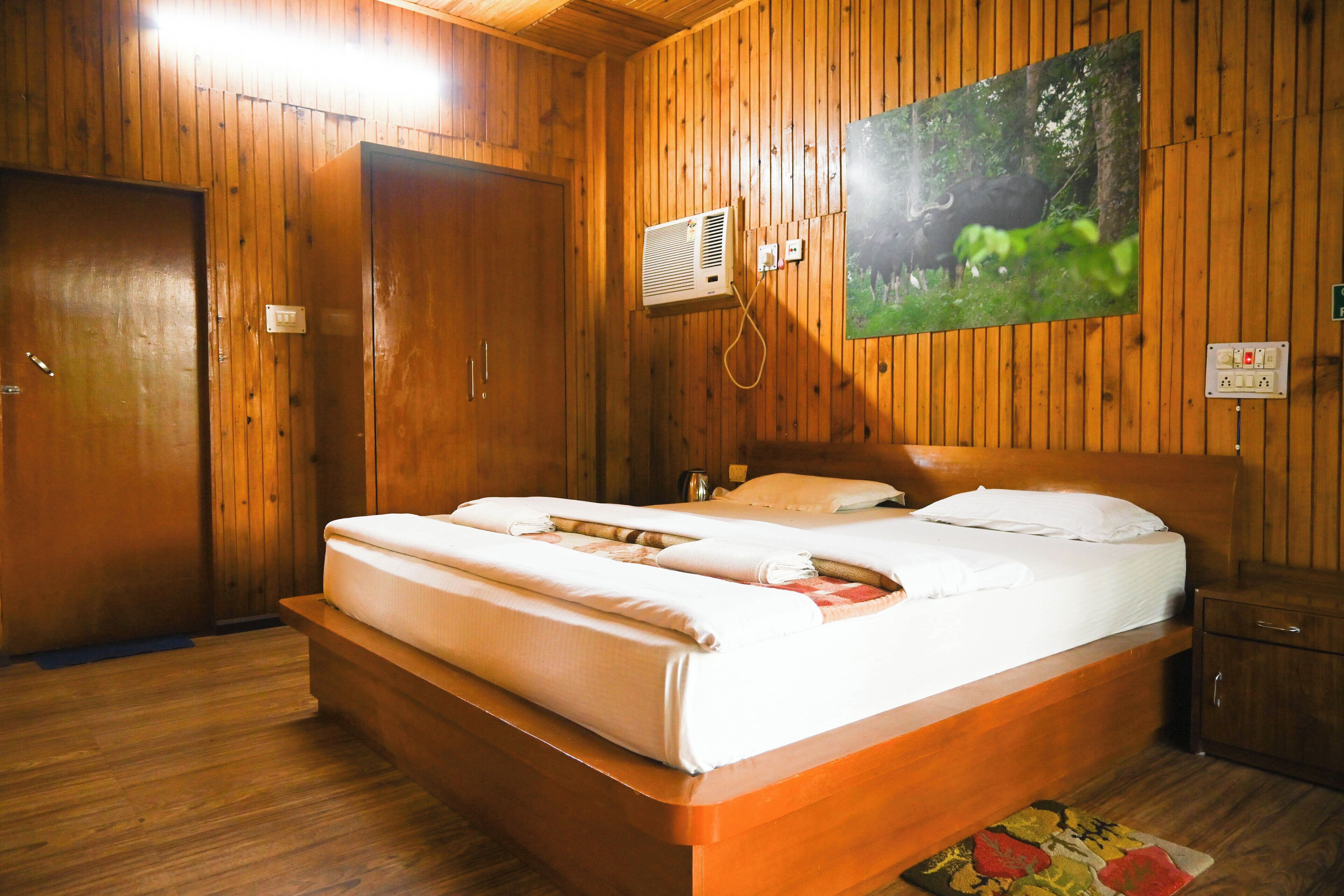 Quarto com painéis de madeira, uma cama, ar condicionado fixado na parede e um quadro de um touro em uma floresta.