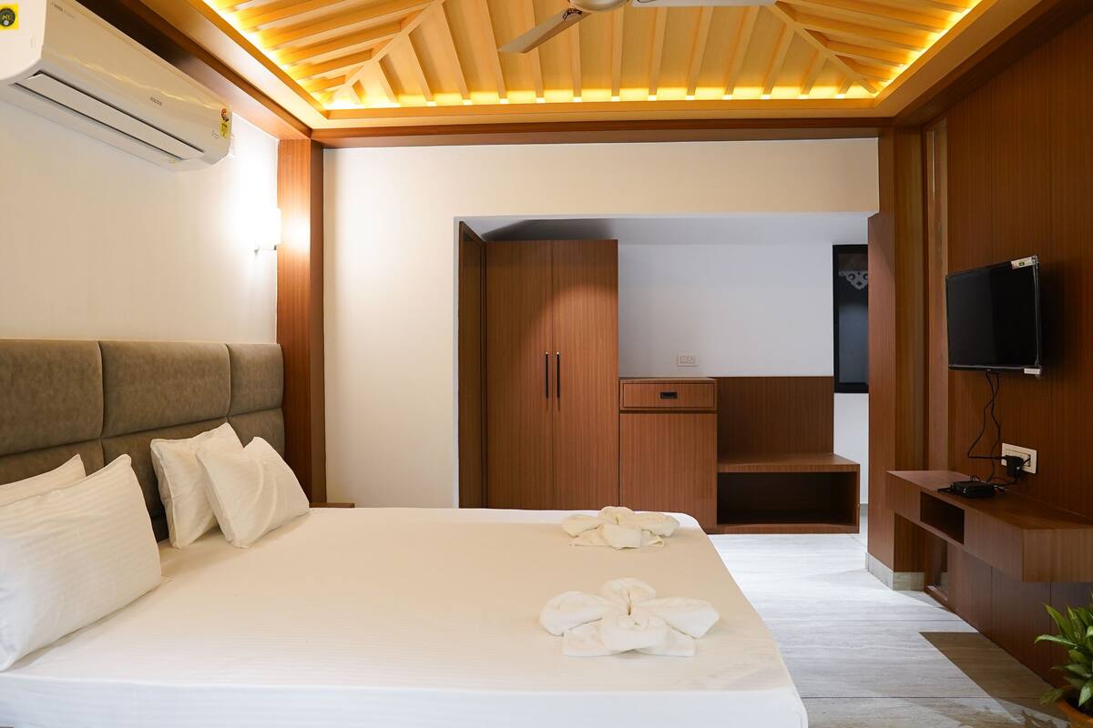 Una habitació d'hotel moderna amb un llit gran, un armari de fusta, una televisió i un ventilador de sostre.