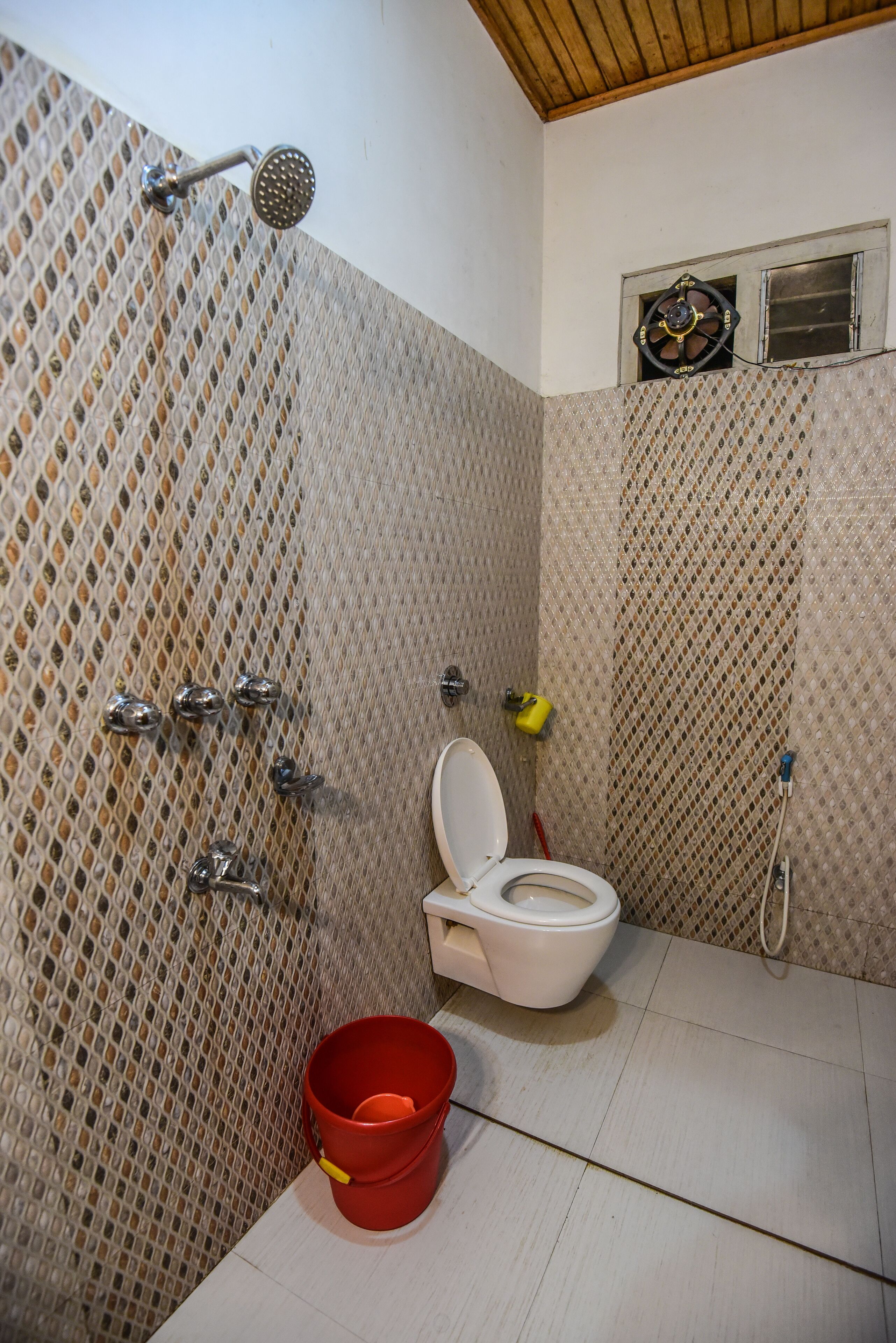 A bathroom with a shower, toilet, and a red bucket.