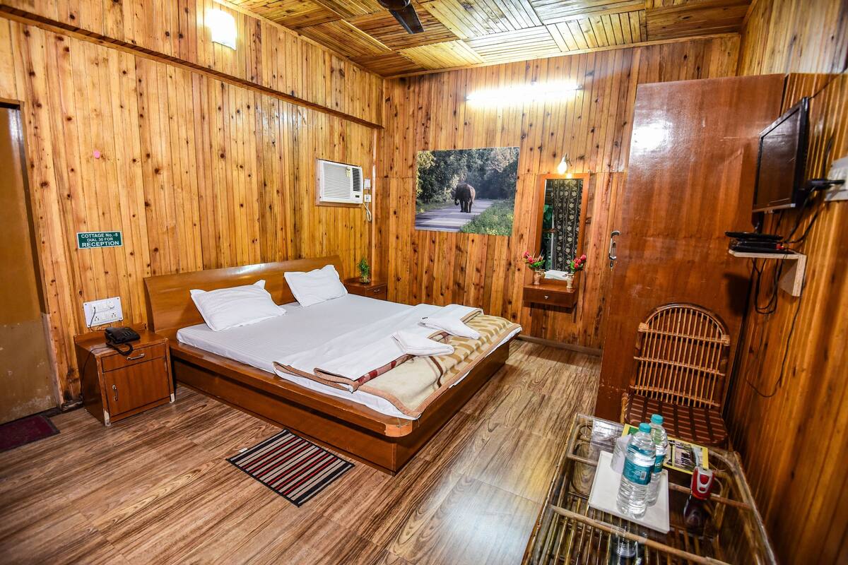 Habitació amb panells de fusta, un llit, una tauleta de nit, una taula petita amb una cadira, una televisió i un quadre a la paret.