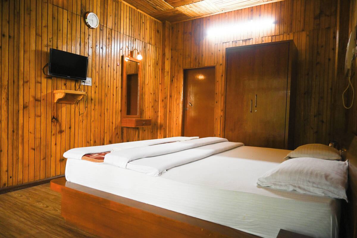 Una habitació amb panells de fusta, un llit, una televisió penjada a la paret i una porta de fusta.