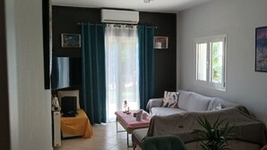 Un salon avec un canapé, une petite table, une chaise, une plante et un tableau accroché au mur.