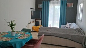Un espace de vie compact comprenant une table à manger, des chaises, un canapé, un téléviseur et une fenêtre avec des rideaux.