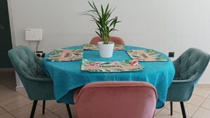 Une table ronde recouverte d’une nappe turquoise, deux chaises turquoise, une chaise rose et une plante en pot.