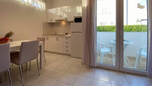 A modern kitchen with white cabinets, a built-in oven, and a dining area with a table and chairs. - Apartments Pulic (Zaboric)
