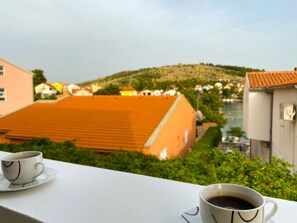Ein Balkon mit zwei Kaffeetassen, mit Blick auf einen Hügel mit Gebäuden.
