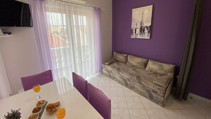 A living room with a sofa, a dining table with breakfast items, and a painting of the Eiffel Tower. - Apartments Pulic (Zaboric)