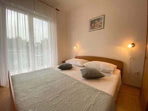 A neatly made bed with patterned bedding, two bedside lamps, and a painting on the wall. - Apartments Pulic (Sibenik)