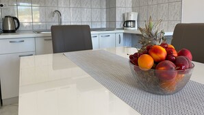 A modern kitchen with white cabinets, a coffee maker, and a fruit bowl on the table. - Apartments Pulic (Zaboric)