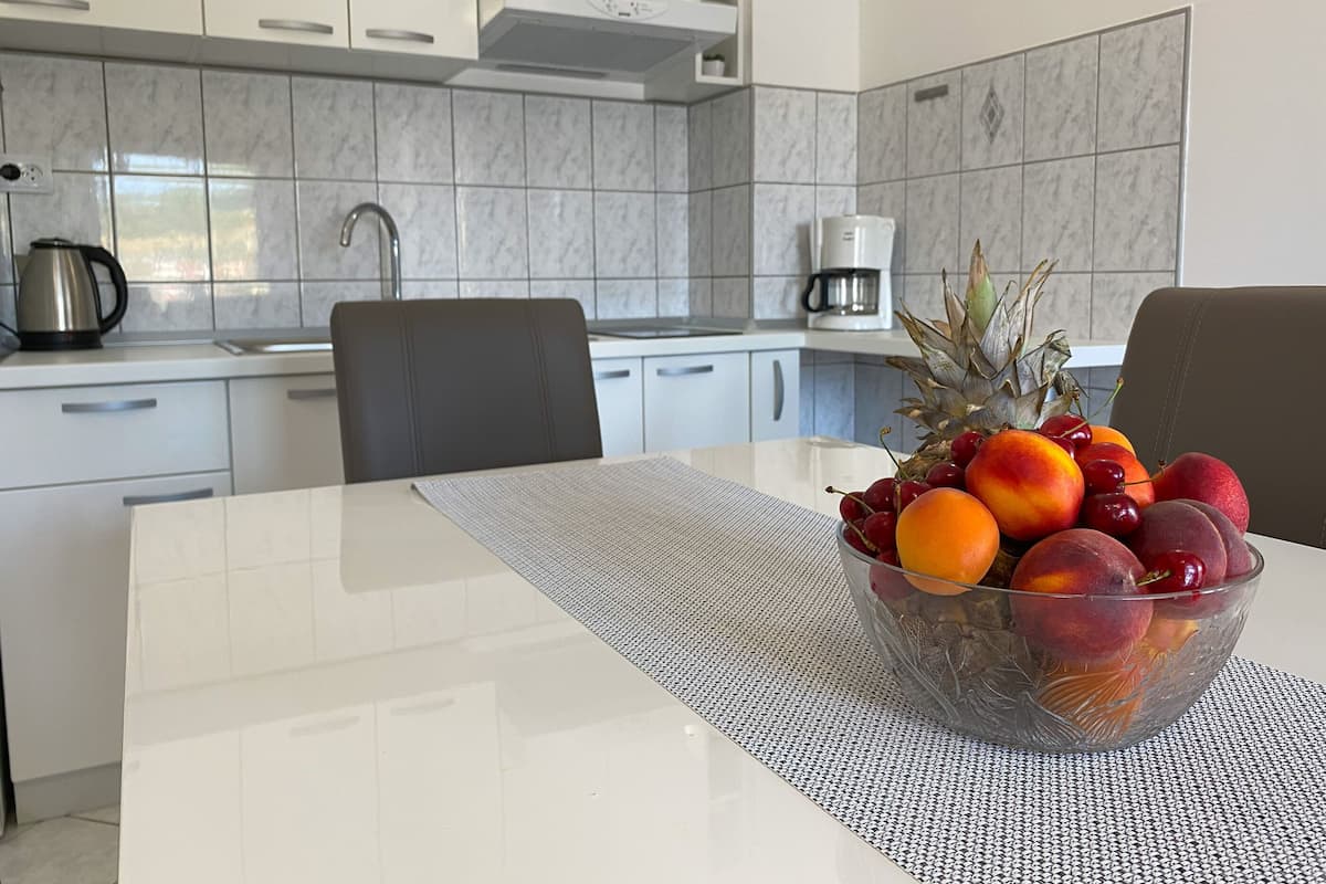Una cucina moderna con mobili bianchi, una macchina da caffè e una ciotola di frutta sul tavolo.