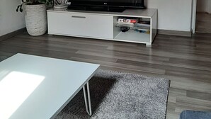 A modern living room with a flat-screen TV on a white entertainment unit, a white coffee table, a grey shaggy rug, and a potted plant. - Apartments Postira uz More (Postira)