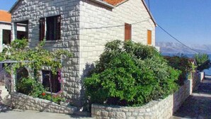 A stone house with a tiled roof, surrounded by greenery and a clear view of the sea. - Apartments Postira uz More (Postira)