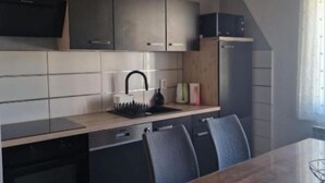 A modern kitchen with dark cabinetry, a wooden countertop, and a dining area with a table and chairs. - Apartments Postira uz More (Postira)