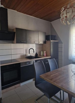 Een moderne keuken met een houten plafond, zwarte kastjes, een betegelde spatwand, en een eethoek met een houten tafel en stoelen.