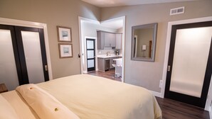 Habitación de hotel con una cama grande, una kitchenette y un baño visible a través de una puerta abierta.