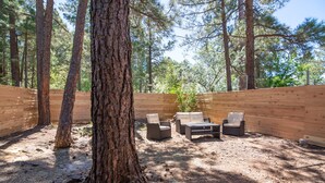 Una terraza de madera con mobiliario exterior, rodeada de árboles altos.