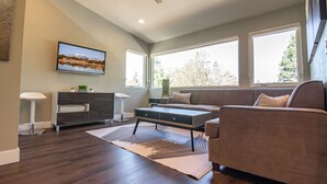 Una sala de estar moderna con un sofá, una mesa de centro, un televisor en la pared y ventanas amplias.