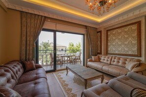 A spacious living room with a large sofa, a smaller sofa, and a coffee table. There is a balcony with a table and chairs outside. - PEARL OF CAPPADOCIA (Avanos)
