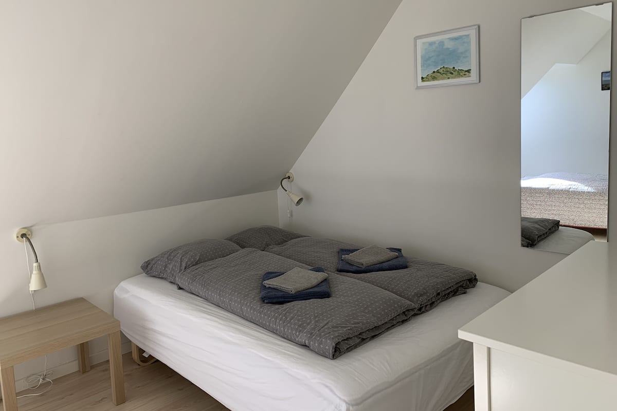 Une chambre à coucher avec un lit, une table de chevet, une lampe, un miroir et un tableau encadré accroché au mur.