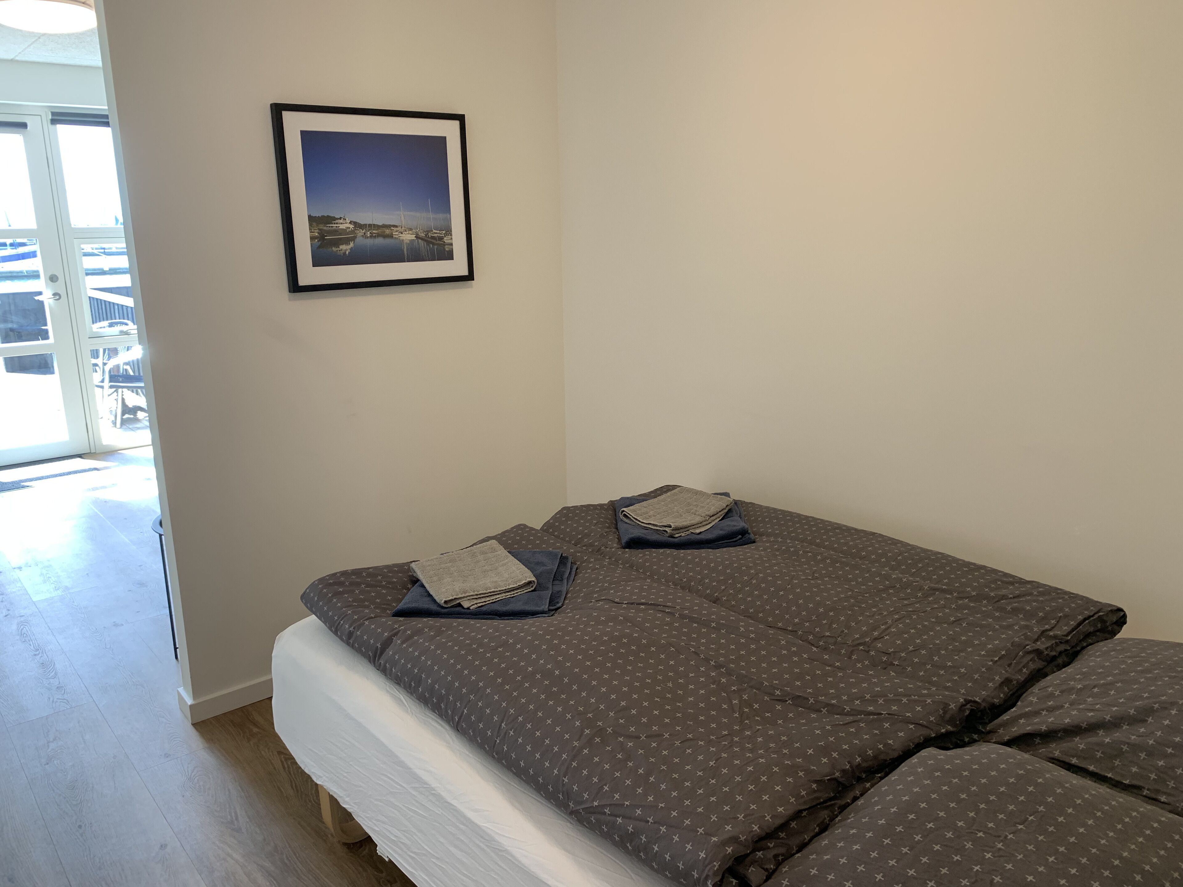 Ein Schlafzimmer mit einem Bett, einem gerahmten Bild an der Wand und Blick ins Freie.