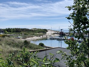 Una marina costera con barcos amarrados, una playa arenosa y un área boscosa al fondo.