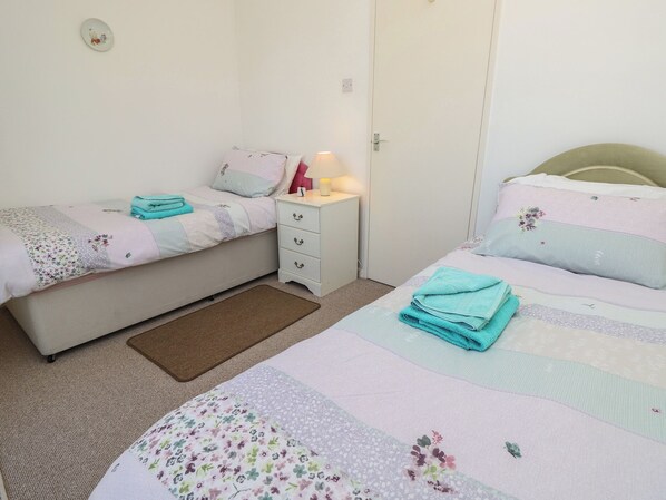 Une chambre avec deux lits, une table de chevet, une lampe et une porte.