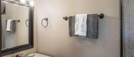 A bathroom with a sink, mirror, towel rings, and a shower curtain.