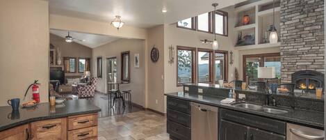 A spacious kitchen with a stone fireplace, wooden cabinets, and a dining area with a view.