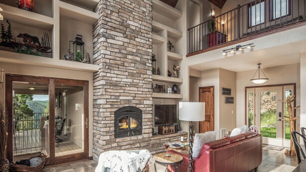 Un salón amplio con chimenea de piedra, un sofá rojo y un balcón con mobiliario de exterior.