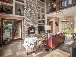 A spacious living room with a stone fireplace, a red sofa, and a balcony with outdoor furniture. - Avalon by Ruidoso Vacation Rentals (Ruidoso)