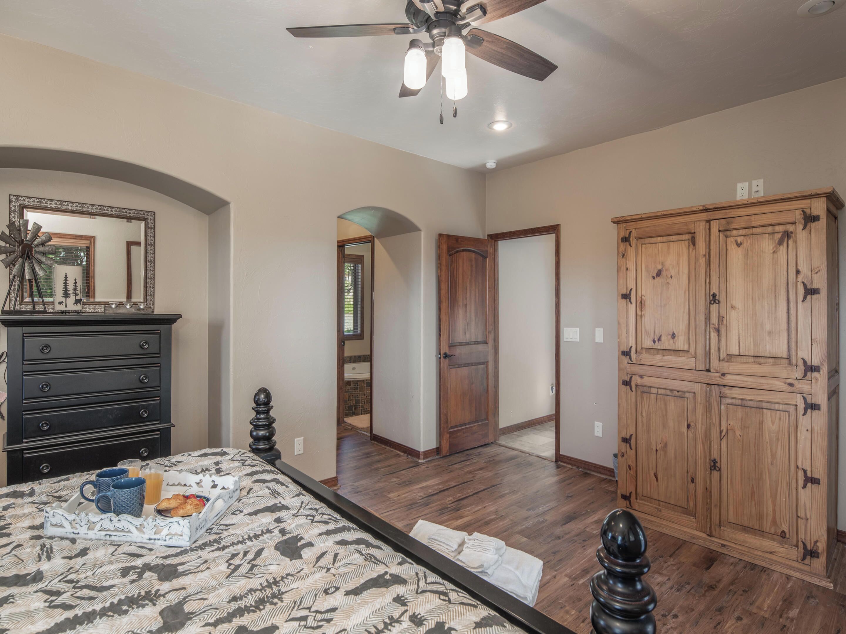 A bedroom with a bed, dresser, wardrobe, and a ceiling fan.