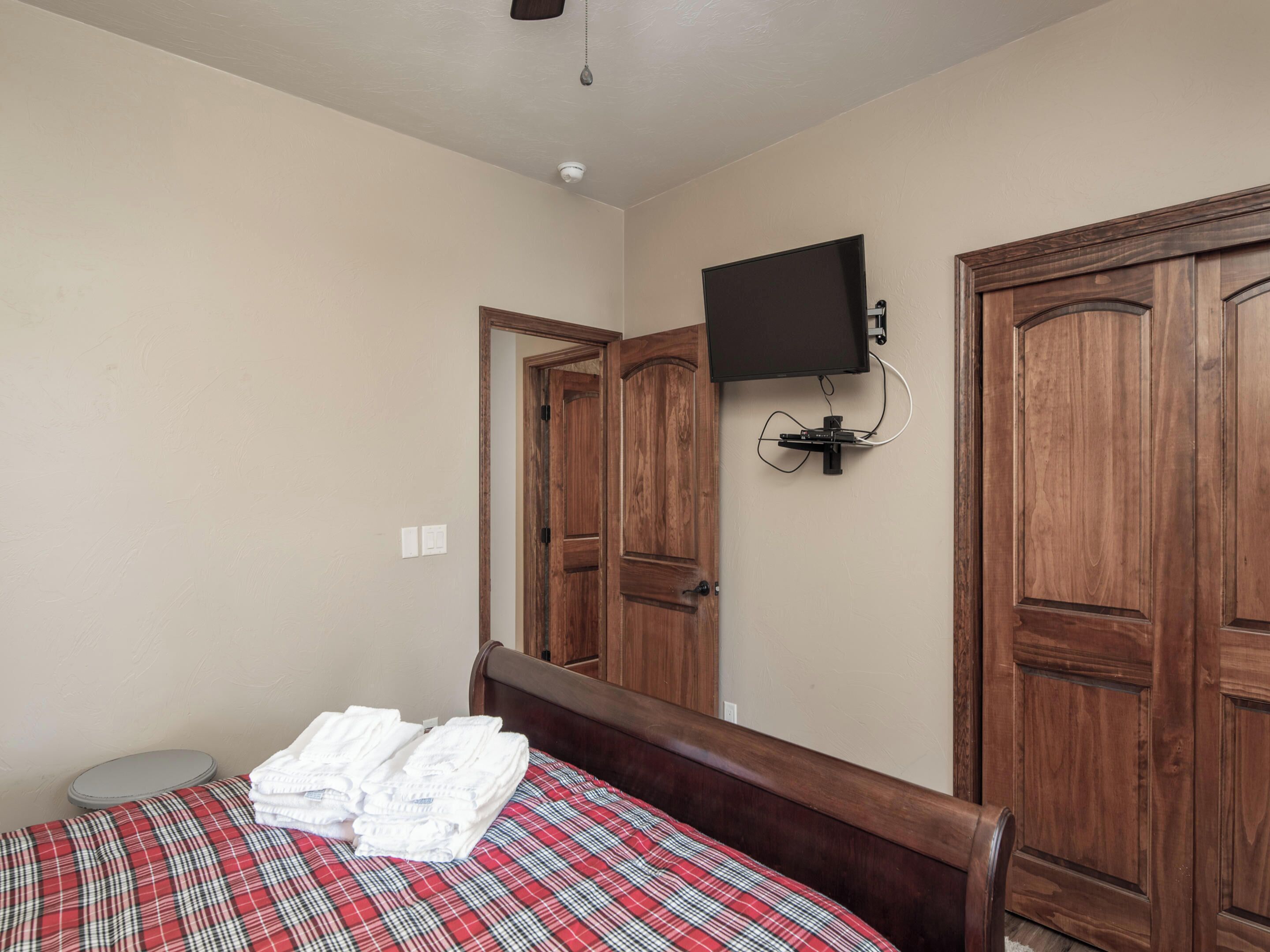 Un dormitorio con una cama, un televisor montado en la pared y puertas de madera.