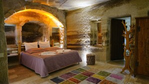 A bedroom with a bed, a wooden arched doorway, a mirror, and a wooden tree-shaped decoration. - Göreme Cave Lodge (Nevsehir)