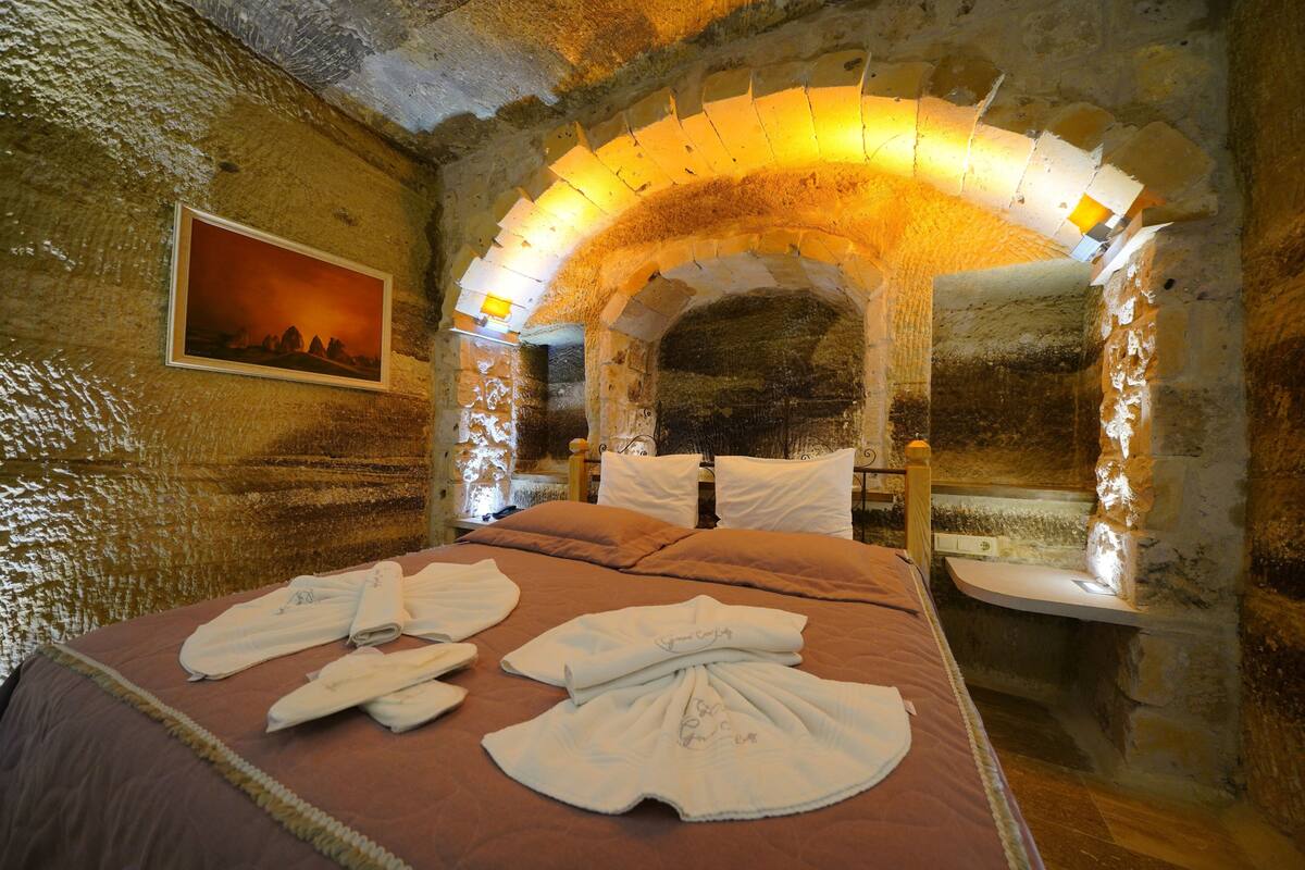 A stone-walled room with a bed, a painting, and a stone archway.