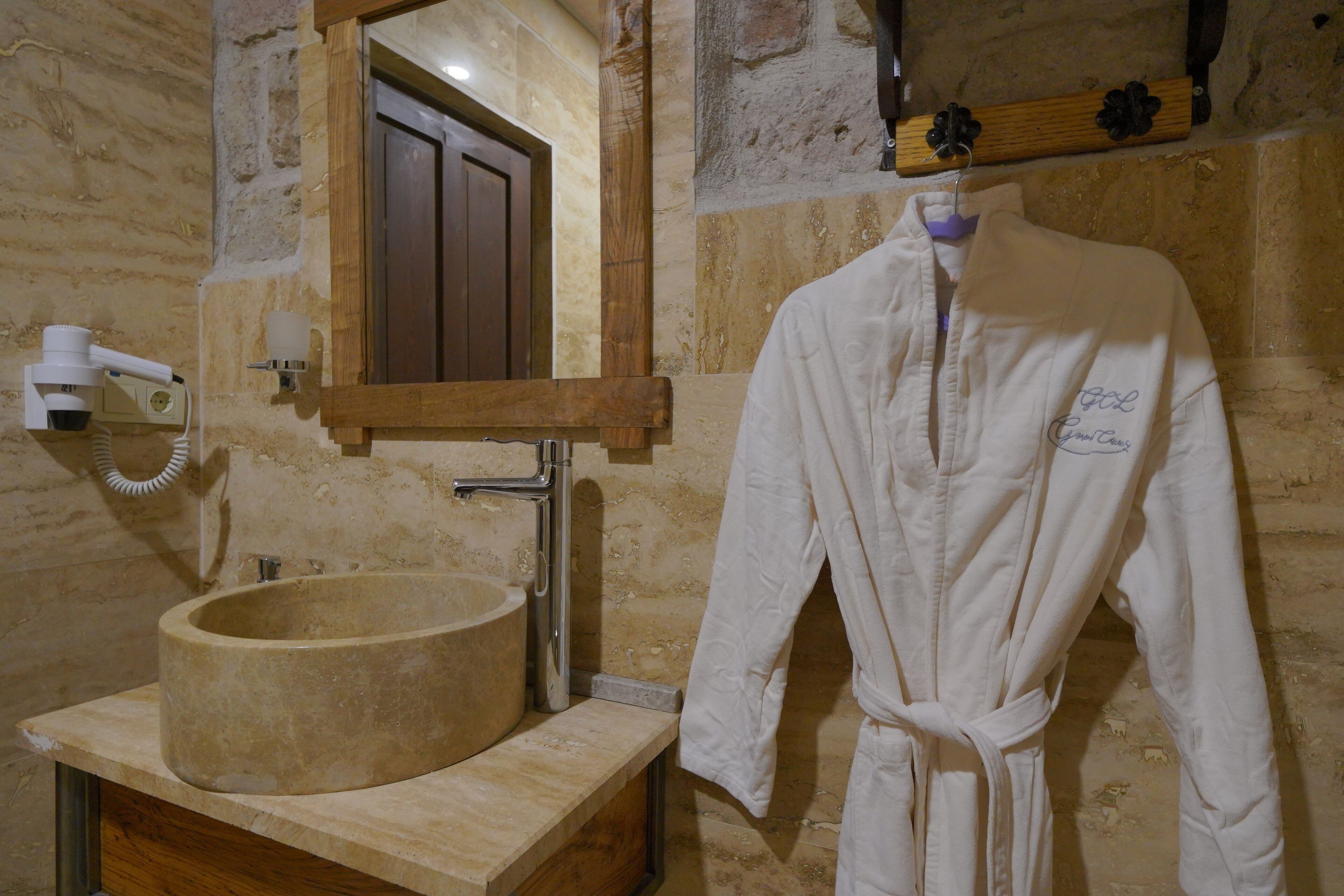 A bathroom with a stone sink, a wooden vanity, a robe hanging on the wall, and a mirror above the sink.