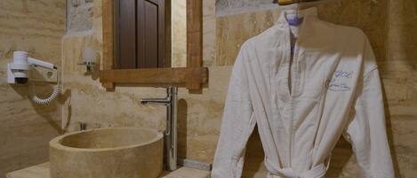 A bathroom with a stone sink, a wooden vanity, a robe hanging on the wall, and a mirror above the sink.