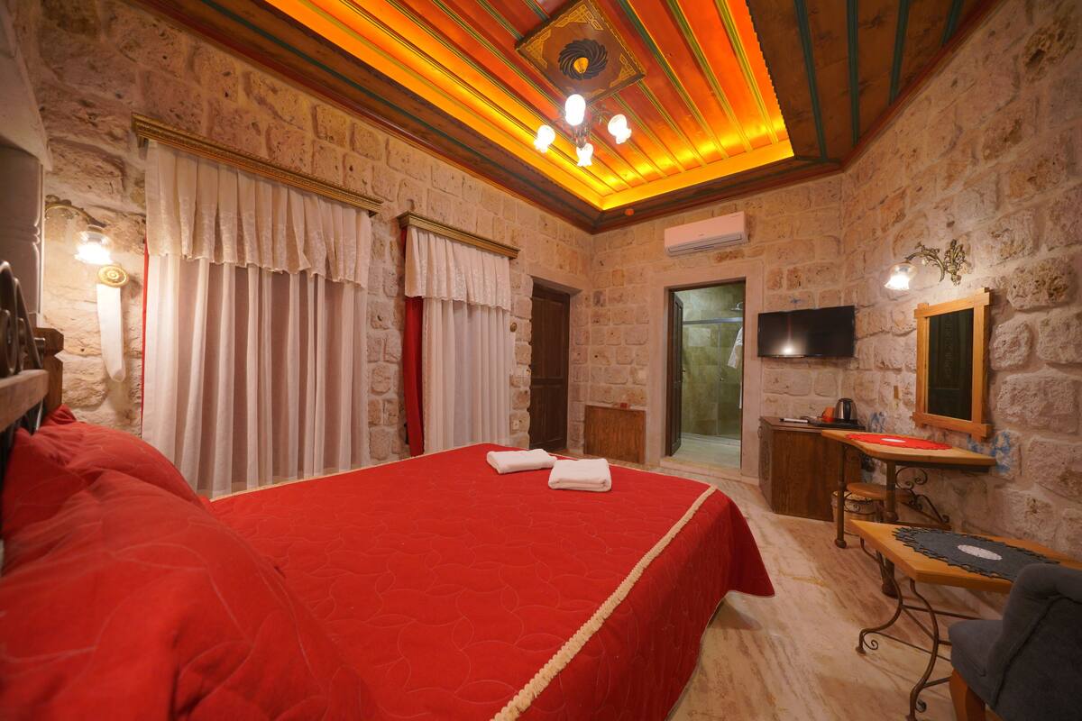 A room with a large bed, a desk, a chair, a television, and a stone wall.