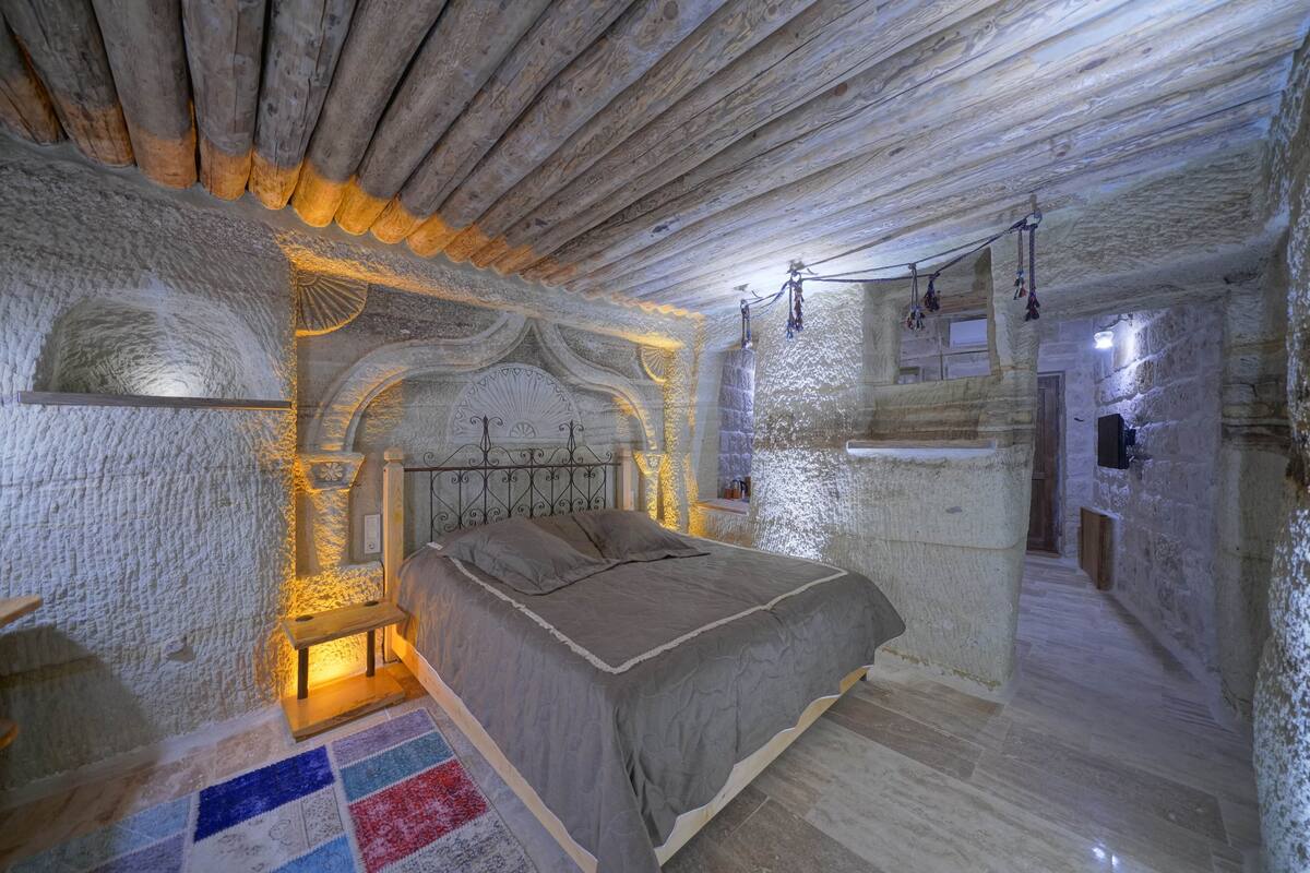 A rustic bedroom with a stone wall, a wooden ceiling, and a bed with a headboard.