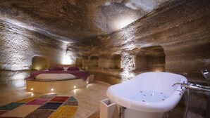 A room with a large bathtub, a bed with a colorful rug, and a unique stone wall. - Göreme Cave Lodge (Nevsehir)