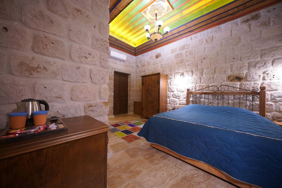 A bedroom with a stone wall, a wooden bed, a colorful rug, and a wooden dresser.